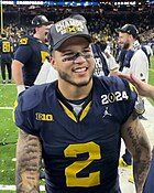 A smiling football player in a baseball hat.