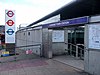 A grey building with a black top and a blue sign reading "CANNING TOWN STATION" in white letters all under a blue sky with white clouds