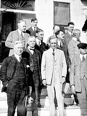 A black and white photograph of about ten white men in three-piece suits standing on the steps of a building with columns