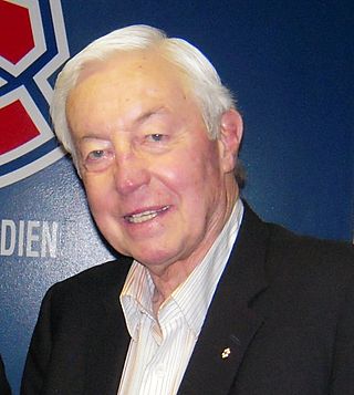 Photo de Jean Béliveau devant le logo des Canadiens de Montréal