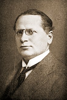 Portrait of a middle-aged man wearing glasses and a suit.