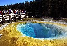 Photographie montrant le bassin coloré de la source Morning Glory Pool, avec des visiteurs à son bord.