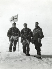 Photo en noir et blanc de trois hommes debout dans la neige, un drapeau britannique planté devant eux.