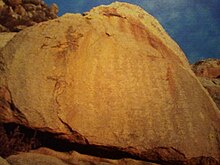 Photograph of an orange rock inscribed with pictorial symbols