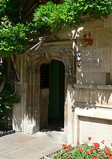 Открытая каменная арка с квадратным верхом, справа цветочная клумба и растущие сверху листья; написано наверху арки «Мужское 2-е Торпид 06»; справа красный дракон держит зеленый флаг над словами 