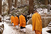 An image of monks in orange robes walking on a stone path with Buddhist monuments in the background.