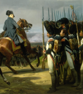 Napoleon, on a horse, looks across a line of bearskinned-hatted troops, one of the soldiers is breaking ranks and holding his hat up gesturing towards Napoleon