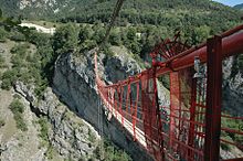 Un étroit pont suspendu peint en rouge passant au dessus d'une profonde gorge.