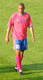 Photographie d'un joueur de football au teint marron, avec un maillot rose, vu de face.