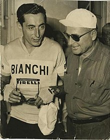 Photo en noir et blanc montrant deux hommes, celui de gauche est en tenue de cycliste, celui de droite plus âgé porte une casquette et des lunettes de soleil.