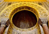 Photographie de la partie supérieure du mihrab. La demi-coupole, coiffant la niche, est réalisée en bois cintré, recouvert d'un enduit épais, et peint d'un décor végétal complexe.