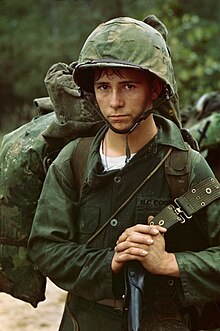 A photograph of a young United States Marine Corps private waiting against the backdrop of a jungle