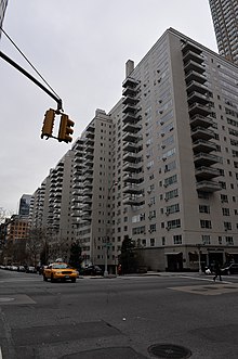 Manhattan House as seen from across the intersection of Third Avenue and 66th Street. The building contains a white-brick facade with projecting glass balconies. There is a taxi on the road to the left.