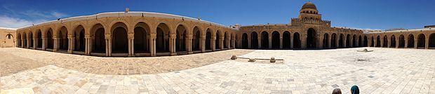 Vue panoramique de la cour entourée de portiques. De gauche à droite : le portique oriental, qui ouvre sur la cour par dix-huit arcades en plein cintre outrepassé, le portique méridional et une partie du portique occidental.