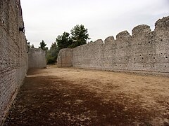 Photographie en couleurs de l'intérieur non cloisonné d'une vaste bâtiment aux murs ruinés en partie haute.