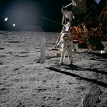 Photo d'un astronaute sur la Lune devant un LEM avec sur sa gauche un collecteur de vent solaire.