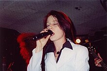 Une femme aux cheveux noir et rouge chante dans un micro.