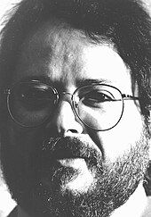 photographie en noir et blanc d'un homme avec lunettes, barbe et moustache.