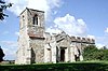 A stone church seen from the southwest, with a tower on the left; the porch and body of the church are battlemented