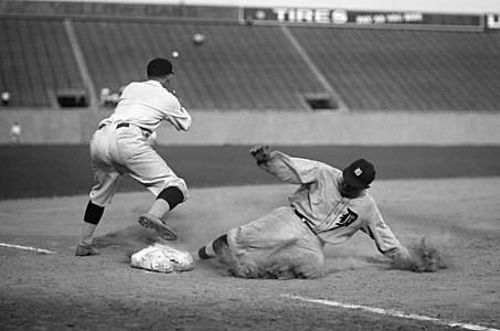 A player slides foot first into a baseball base, kicking up dirt with his leg and with an arm he has on the ground