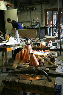 Photographie d’un atelier où figurent des objets en cuivre jaune.