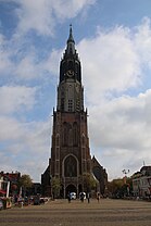 Photographie en couleurs d'un clocher d'église et de son drapeau municipal.