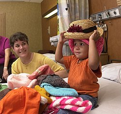 فتاة تحاول تجربة ارتداء القبعات بعد تعرضها لـ علاج كيميائي إثر إصابتها بورم ويلمز، وهو نوع سرطان يصيب الأطفال عادةً.[1]