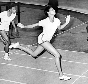 A woman in a T-shirt and shorts, crossing the finish line of a race in first place, ahead of a competitor