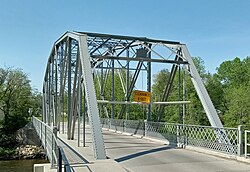 One-lane bridge with metal trusses over a wooden deck, with a pedestrian walkway on the right