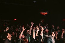 A crowd reaches for a frisbee that is being thrown from a stage.