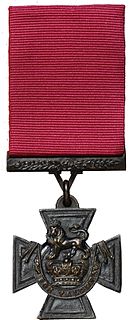 a bronze Cross pattée suspended from a crimson ribbon