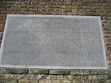 Photographie en couleurs d'une plaque rectangulaire en pierre gris clair incorporée à un mur en brique et portant des inscriptions.