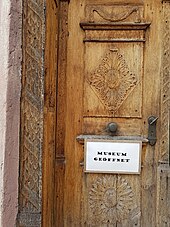 An der unbemalten, hölzernen Doppeltür hängt ein Schild mit den Worten „Museum geöffnet“.