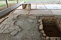 Vue d'une cour antique partiellement dallée ; une cave s'ouvre dans la cour.