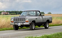 Un Dodge Ram de couleur grise roulant sur la route. Il y a deux personnes dans le véhicule, qui porte une plaque d'immatriculation allemande.