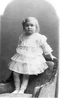 Photographie de Lidia Zamenhof, en 1907, debout sur un fauteuil, avec une robe et une nœud dans les cheveux.