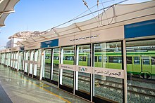 A metro train platform at Jamarat, the station closest to the city walls. There is a green metro train travelling in the opposite direction on the opposite platform.