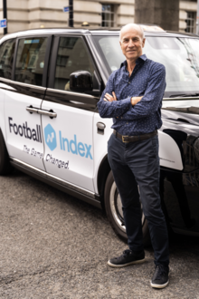 Адам Коул, основатель Football Index, стоит рядом с такси с логотипом Football Index.
