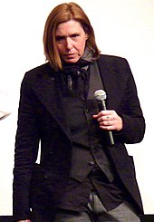 Женщина-музыкант, Пэтти Шемел, в черном костюме, держит микрофон.