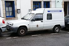 Foto eines weißen Kleintransporters vom Typ Renault Express (auf Basis des Kleinwagens Renault 5). Das Auto ist von schräg vorne aufgenommen, es steht am Straßenrand geparkt vor einem Gebäude. Auf der Fahrertür sind Name und Wappen der Stadt Pont-Aven angebracht. Am Kastenaufbau befindet sich ein blauer Schriftzug „Police municipale“ in Versalien. Die Fahrzeugvorderseite ist völlig neutral ohne Markierungen. Das Auto verfügt nicht über Blaulicht oder sonstige Kennleuchten. Sein Kennzeichen ist 7181 YH 29.