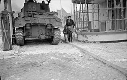 Een Nederlandse vader brengt zijn kinderen in veiligheid langs een Sherman tank tijdens de gevechten in 's-Hertogenbosch