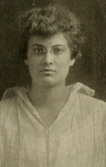 A young white woman with wavy hair, wearing eyeglasses and a white collared shirt