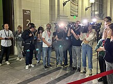 Photographie en couleurs représentant un groupe de personnes (journalistes) dans la salle des pas perdus du tribunal de Pau.