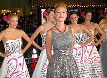 Heigl in a grey and silver dress, behind her several woman wearing the same white dress from the film poster