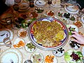 Neben den Köstlichkeiten auf kleinen Tellern steht diese Tajine im Mittelpunkt: ein ursprünglich in al-Andalus beheimatetes Schmorgericht aus Lammfleisch, Safran und Baharat und viel Olivenöl aus der Gegend von Meknes. Die grünen Oliven verleihen dem Gericht eine besondere Note. Man achte auf die Hand rechts im Bild; man isst in Marokko meistens mit der rechten Hand. Hier beginnt der "Angriff".