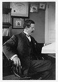 Robert Ridgway sits at his desk. His hand is blackened from the arsenic used to preserve the bird skins.