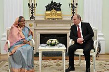 A seated Sheikh Hasina and Vladimir Putin smile at each other across a small table