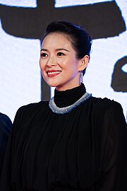 A short-haired woman wearing a black outfit along and a white and blue necklace poses for the camera