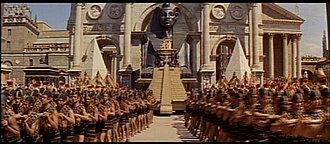 Photogramme d'un péplum, montrant un trône égyptien géant tracté par des esclaves, entrant dans Rome.