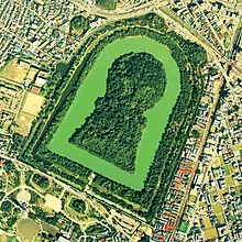 Photo couleur d'un tumulus vu du ciel, demi-ellipse de verdure au milieu d'une zone urbaine.